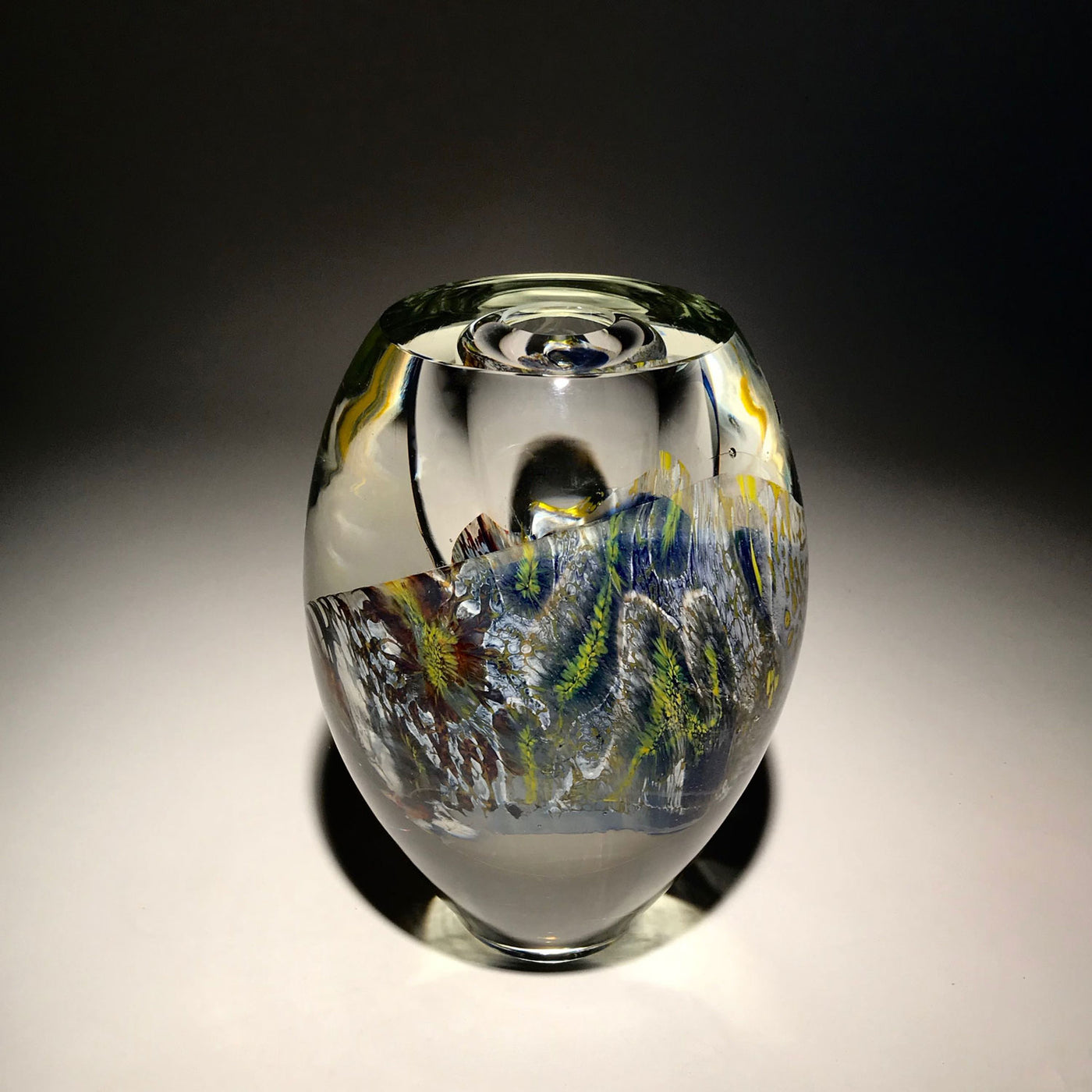 Sculpture d'un vase de couleur transparent, blanc, bleu, jaune et autres réalisé en verre soufflé travaillé à froid par l'artiste Maryse Chartrand de Sutton, Québec, Canada.