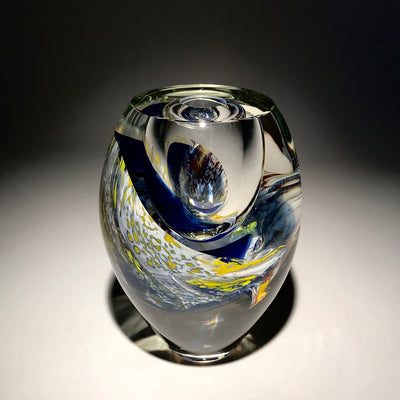 Sculpture d'un vase de couleur transparent, blanc, bleu, jaune et autres réalisé en verre soufflé travaillé à froid par l'artiste Maryse Chartrand de Sutton, Québec, Canada.