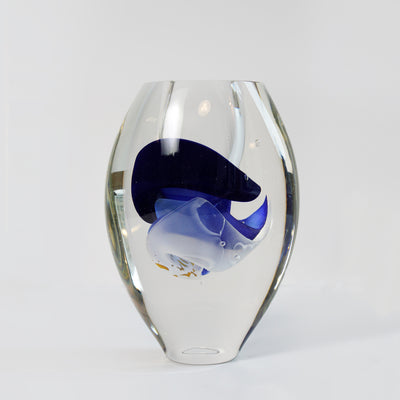 Flottante bleu nuit, réalisé en verre soufflé travaillé à froid par l'artiste Maryse Chartrand de Sutton, Québec, Canada. La technique utilisée donne à ce vase  un effet optique unique où les couches de couleur bleues et blanches semblent flotter dans la paroi intérieure du verre transparent. 