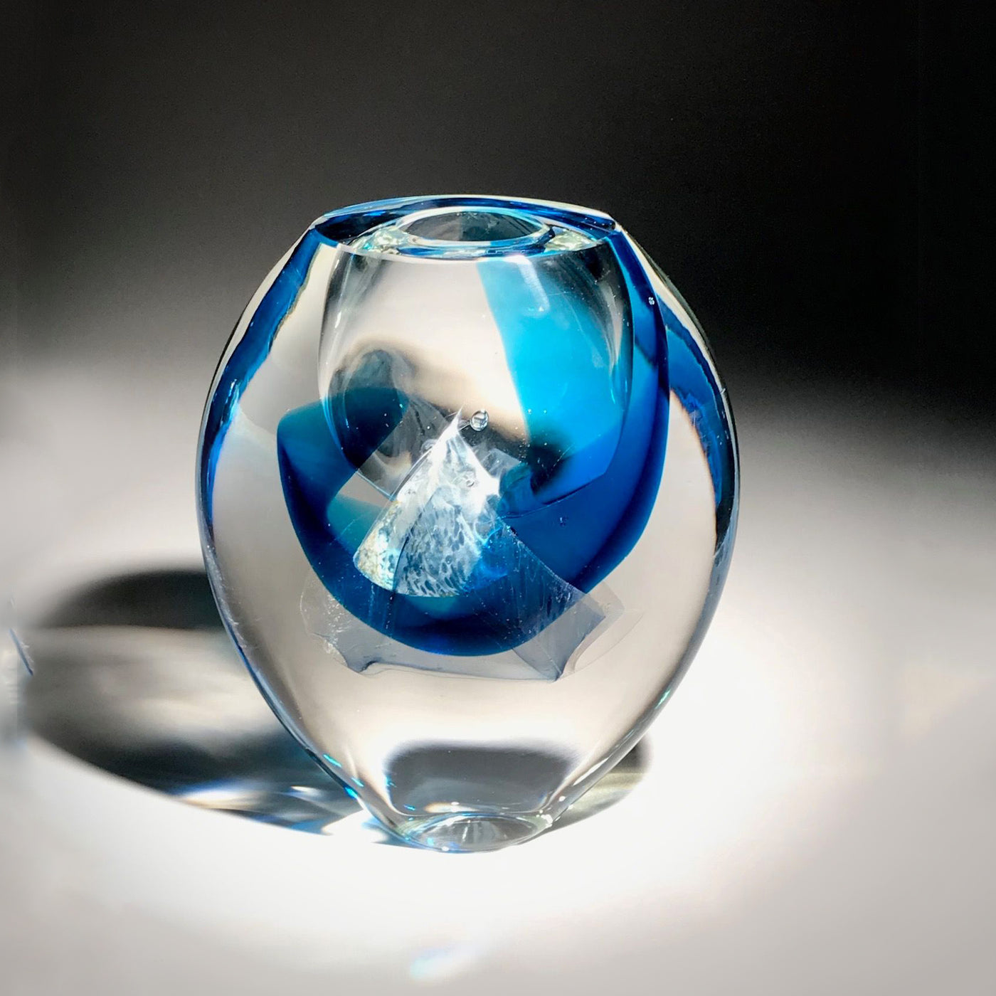 Sculpture d'un vase de couleur transparent, bleu, et blanc réalisé en verre soufflé travaillé à froid par l'artiste Maryse Chartrand de Sutton, Québec, Canada.